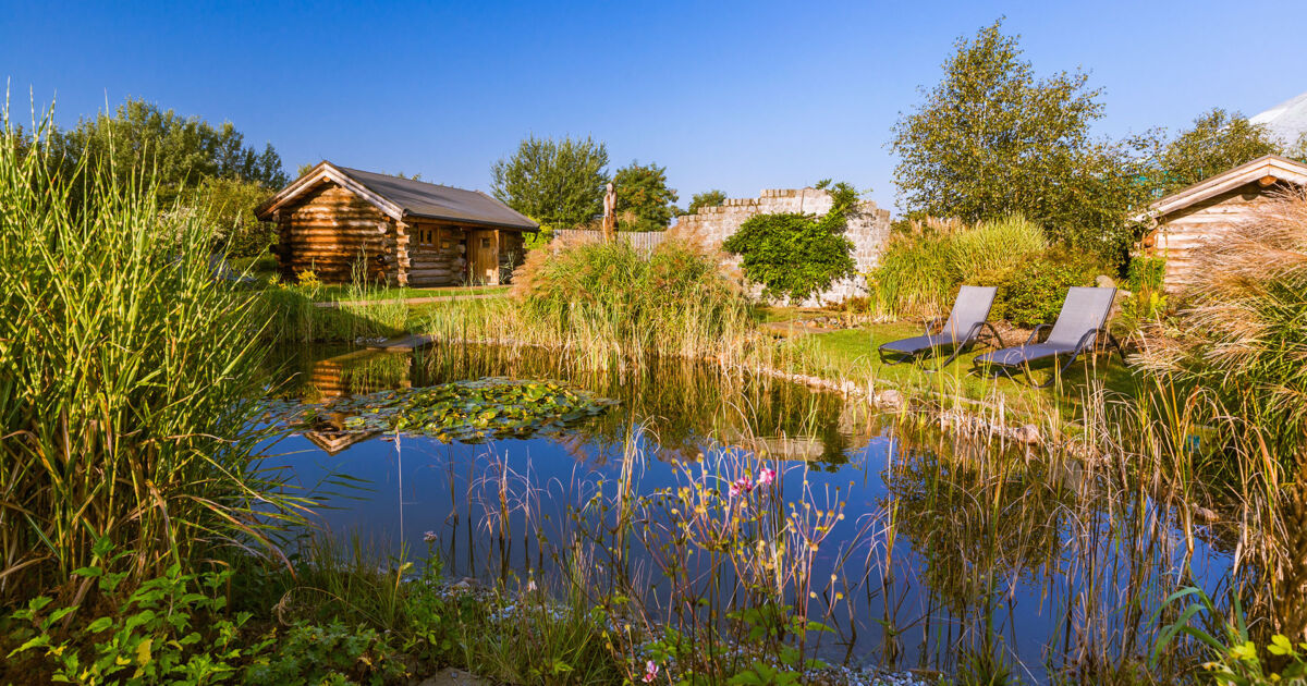 An unserem idyllischen Gartenteich im Saunadorf können Gäste entspannt auf den Relaxliegen die Sonne genießen.