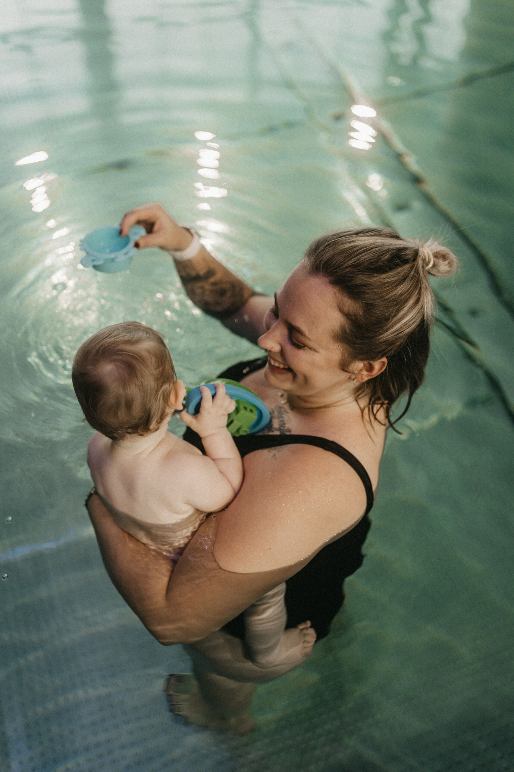 Eine junge Mutter spielt im wohlig warmen Wasser mit ihrem Baby auf dem Arm