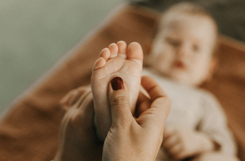 Die Hand einer Hebamme massiert sanft den kleinen Fuß eines auf dem Rücken liegenden Babys