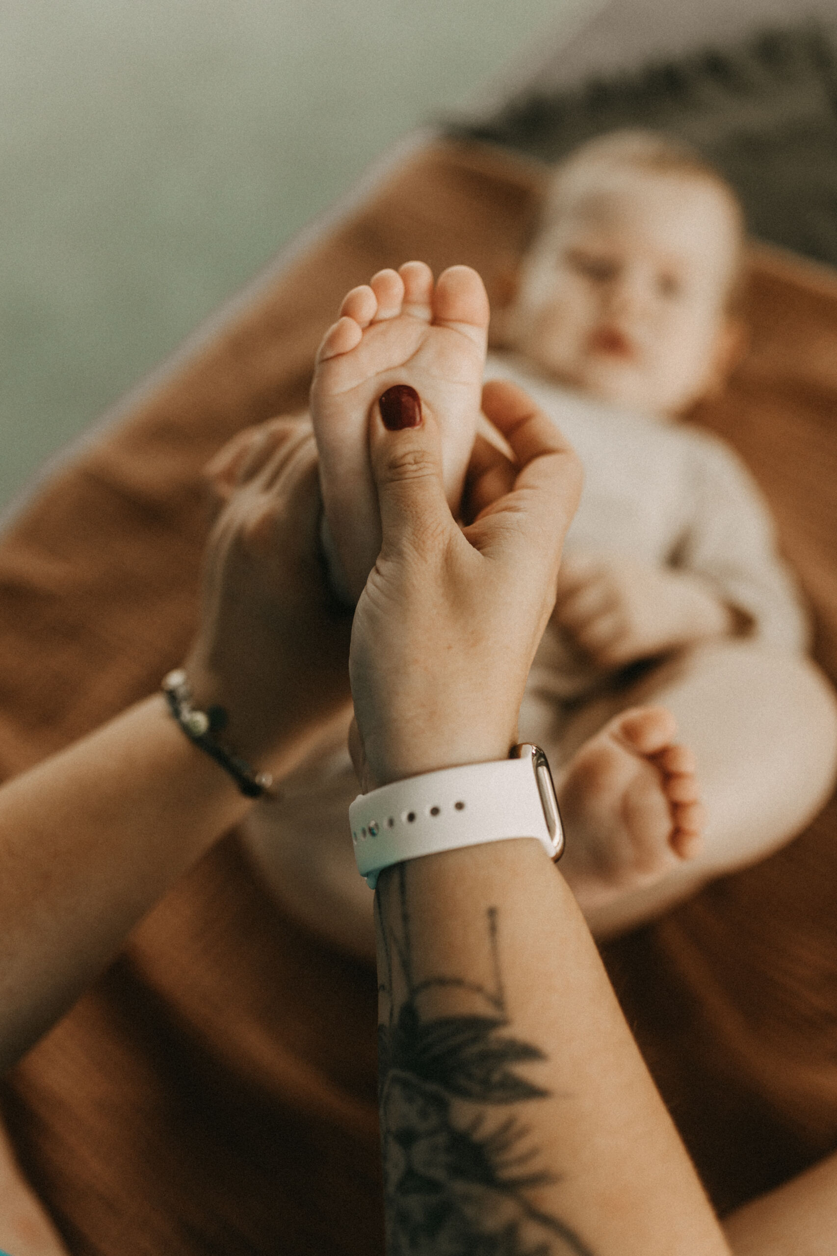 Die Hand einer Hebamme massiert sanft den kleinen Fuß eines auf dem Rücken liegenden Babys